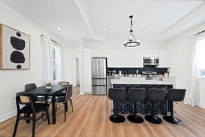 Cozinha moderna com armários brancos, eletrodomésticos de aço inoxidável e uma ilha preta com banquetas.
