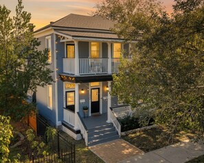 Een woonhuis met twee verdiepingen, een voortuin, balkon en een zichtbaar huisnummer.