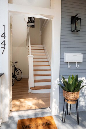 A staircase leading to a second floor, a welcome mat, a potted plant, and a mailbox on the exterior wall.