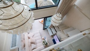A high-ceilinged room with a large window overlooking a pool area, a sofa with cushions, and a decorative hanging light fixture.