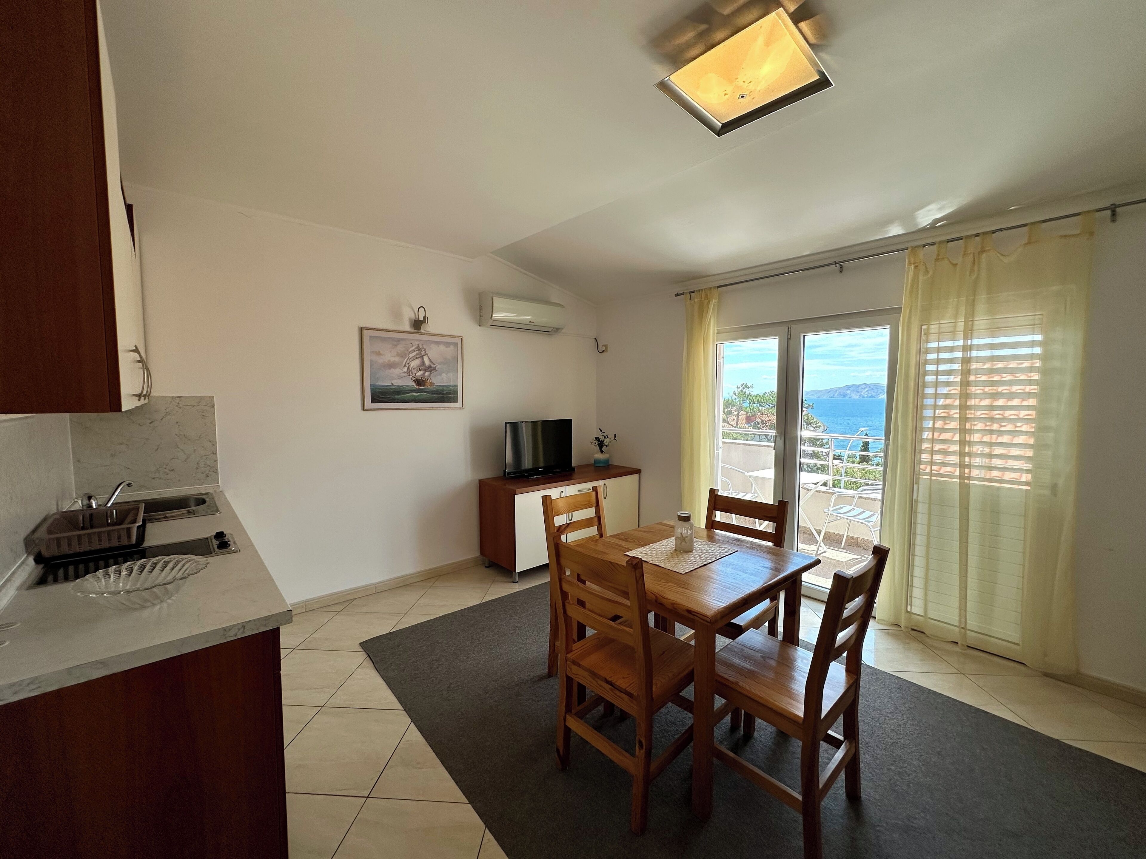 A compact living space with a dining area, kitchenette, and a balcony with a view.
