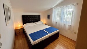 A bedroom with a bed, a nightstand, a window with blinds, and a picture on the wall. - Apartment Velvet Vista 5 (Novi Vinodolski)