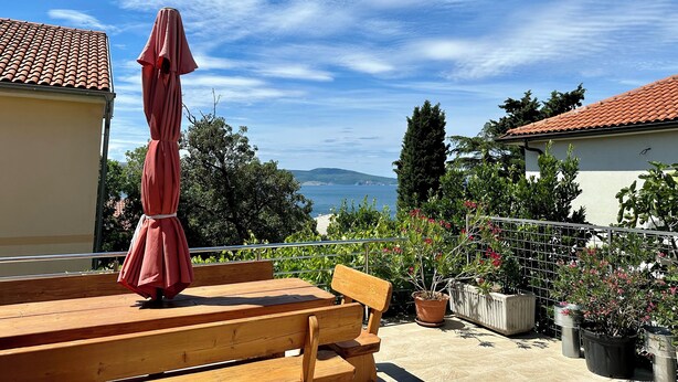 A wooden bench and a red umbrella on a balcony overlooking a body of water with mountains in the distance. - Apartment Velvet Vista 5 (Novi Vinodolski)