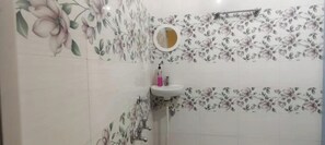 A bathroom with floral wallpaper, a sink with a mirror, and a shower area.