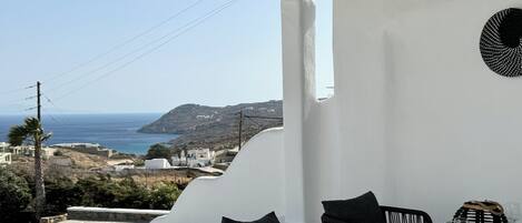 A balcony with a white table set for dining, black chairs, and a view of the sea and hills.