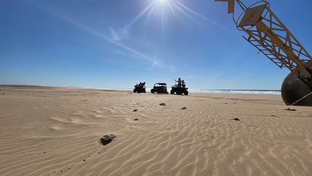 A desert landscape with a clear sky, a large sun, and three off-road vehicles on the sand. - The Maison Bleu room (TANGER)