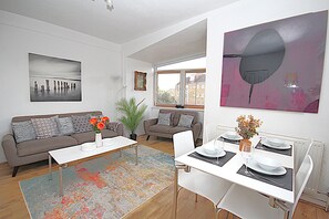 Una sala de estar moderna con comedor, que incluye un sofá, una mesa de centro y una mesa de comedor preparada para cuatro personas.