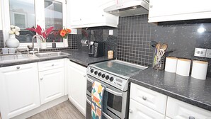 A modern kitchen with white cabinets, a black countertop, a stove, and a window with decorative flowers. - Boutique Apartment minutes to London Bridge Tube (London)
