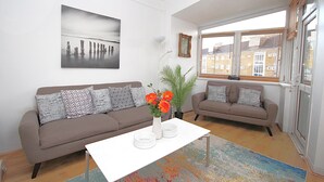 A living room with two sofas, a coffee table, a vase with flowers, a framed picture on the wall, and a window with blinds. - Boutique Apartment minutes to London Bridge Tube (London)