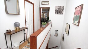 A hallway with a wooden handrail, a white bucket, a patterned rug, and various framed pictures on the walls. - Boutique Apartment minutes to London Bridge Tube (London)