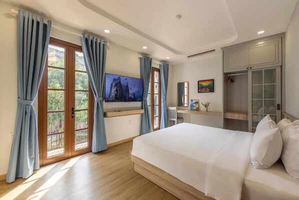 A hotel room with a large bed, a TV mounted on the wall, a desk with a chair, and a wardrobe. - La Maison De Dino Hotels & Apartments  (Phu Quoc)