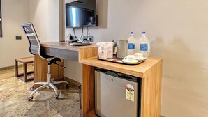 A hotel room with a desk, chair, television, and a small refrigerator. - THE GRAND KD HOTEL (Dabhoi)