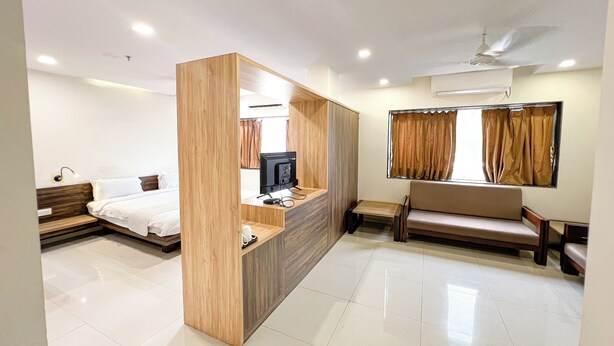 A modern hotel room with a wooden partition, a bed, a sofa, a TV, and an air conditioning unit. - THE GRAND KD HOTEL (Dabhoi)