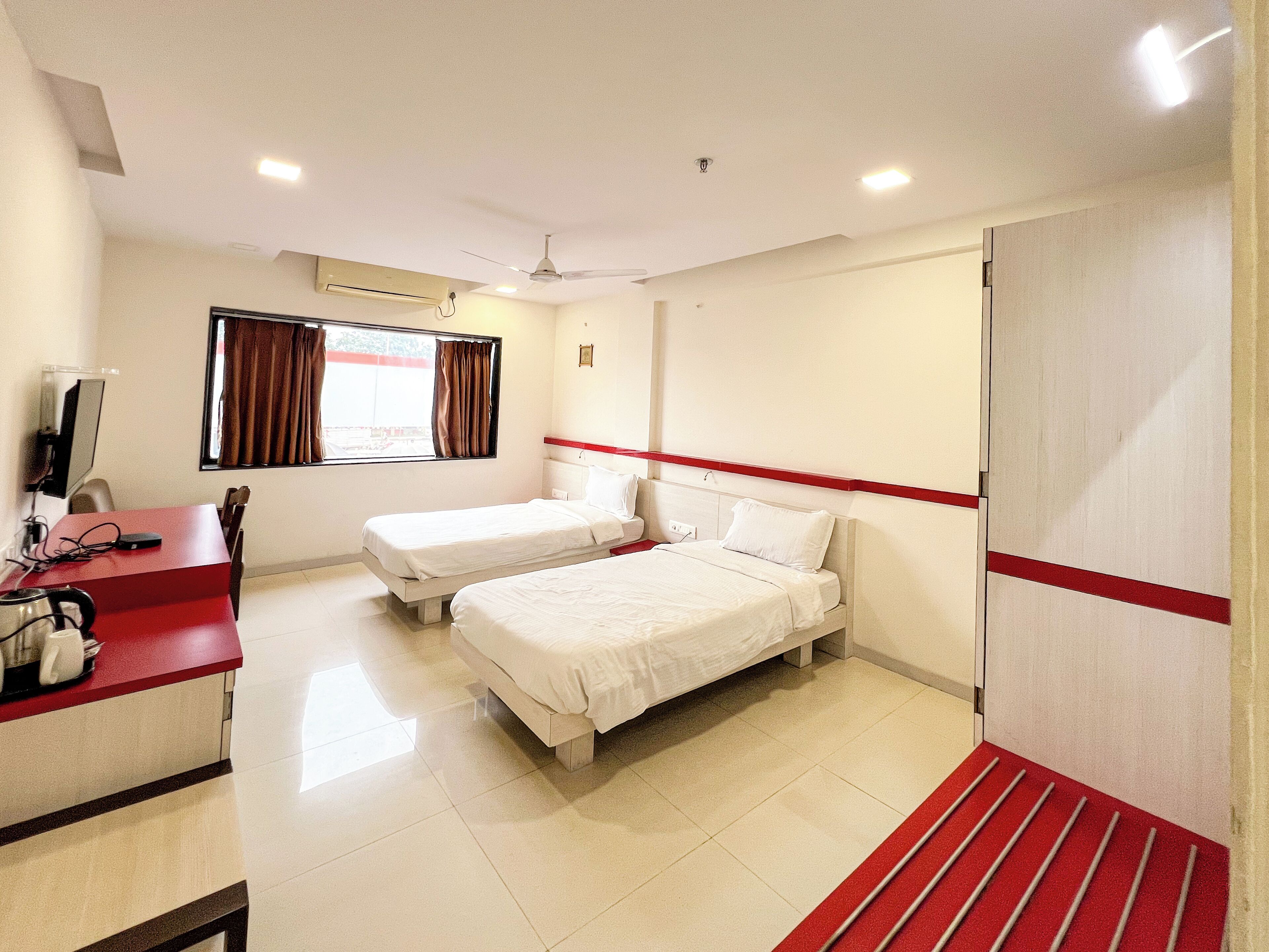 A hotel room with two beds, a desk with a computer, and a window with curtains.