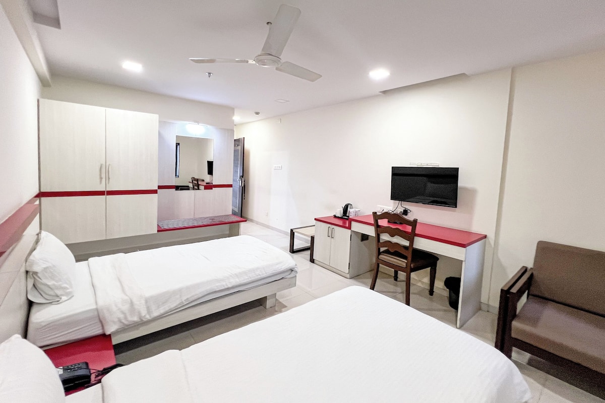 A hotel room with two beds, a desk, a chair, a television, and a ceiling fan.
