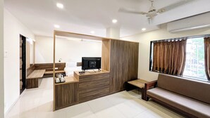 A modern hotel room with a sofa, a TV, a small table, and a kitchenette area. - THE GRAND KD HOTEL (Dabhoi)