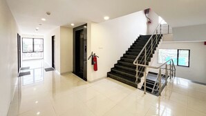 A modern hotel lobby with a staircase, a fire extinguisher, and a view of the outside through a large window. - THE GRAND KD HOTEL (Dabhoi)