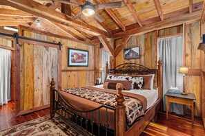 A wooden bedroom with a bed, a nightstand, and a ceiling fan. - Texas Saw Mill (Cabin #1) - Hot Tub & 10 Mins to Main St (Fredericksburg)