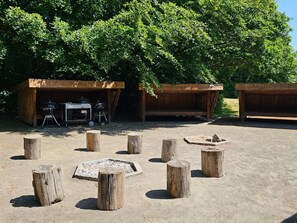 A rustic outdoor area with wooden structures, a barbecue setup, and fire pits.