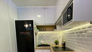 Cocina compacta con muebles blancos, un refrigerador negro, encimera de madera y salpicadero blanco de azulejos.