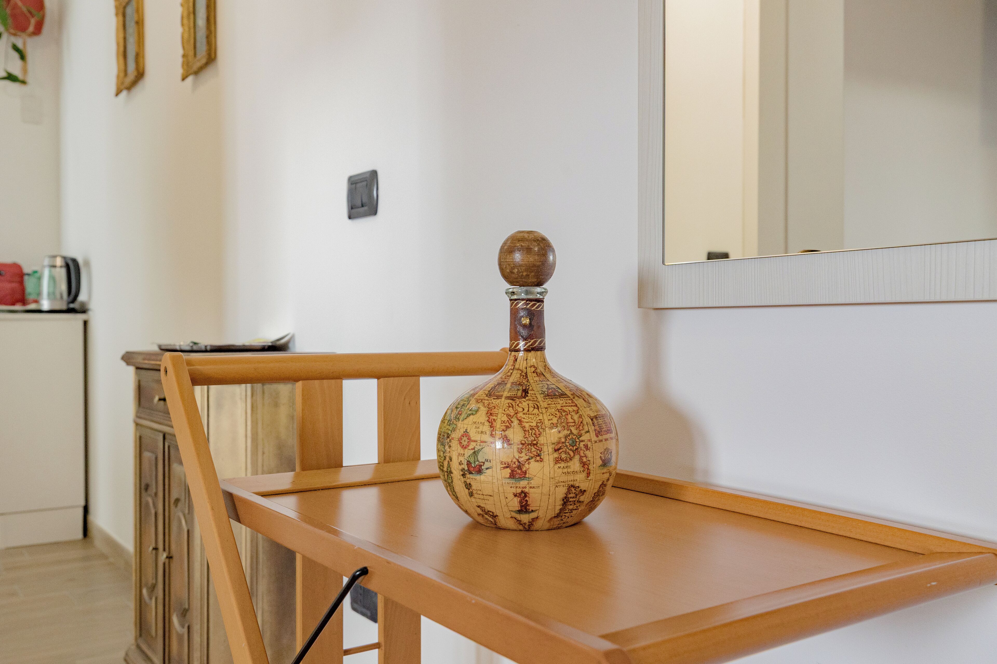 Une chaise en bois, avec un globe posé sur une table, dans une pièce où se trouvent un buffet en bois et un miroir au mur.