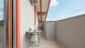 A narrow balcony with a glass door, a small table, and a potted plant.