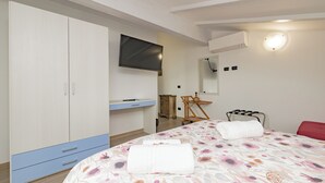 A bedroom with a bed, a wardrobe, a desk, a chair, a TV, and a mirror.