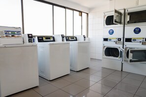 A laundry facility with multiple washing machines and dryers, a control panel, and a window providing natural light.