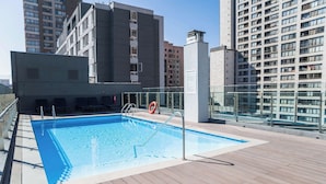 En pool på taget med træterrasse, omgivet af høje bygninger.
