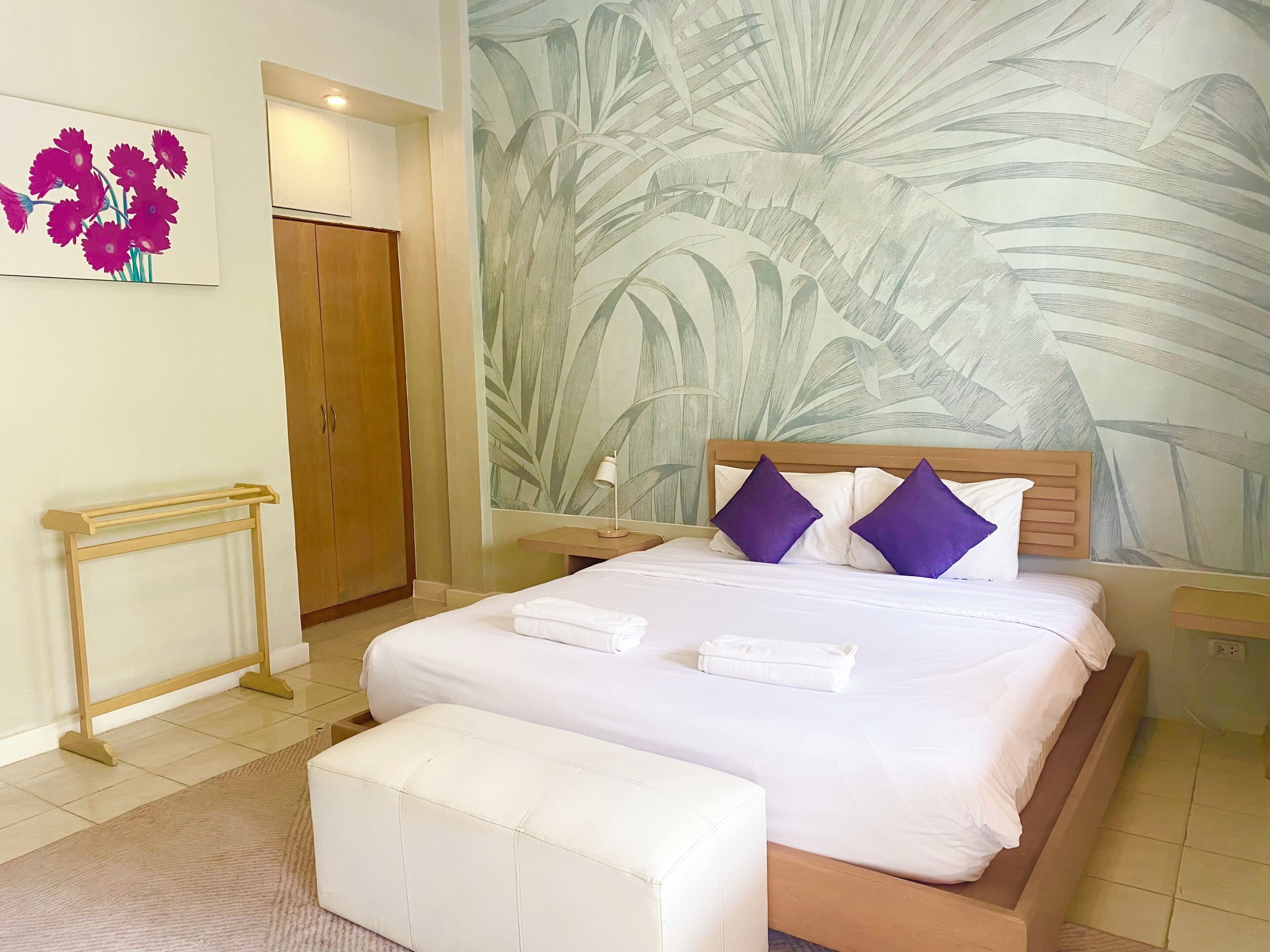 A bedroom with a bed, a wooden headboard, a nightstand, a wall-mounted lamp, and a door.