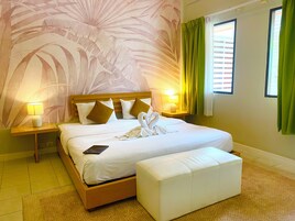 Habitación de hotel con cama, lámpara de noche, una computadora portátil, un reposapiés blanco y una pared con estampado de hojas.
