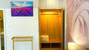 Una habitación con un armario de madera, una mesita, una lámpara de pared y un cuadro de un campo.