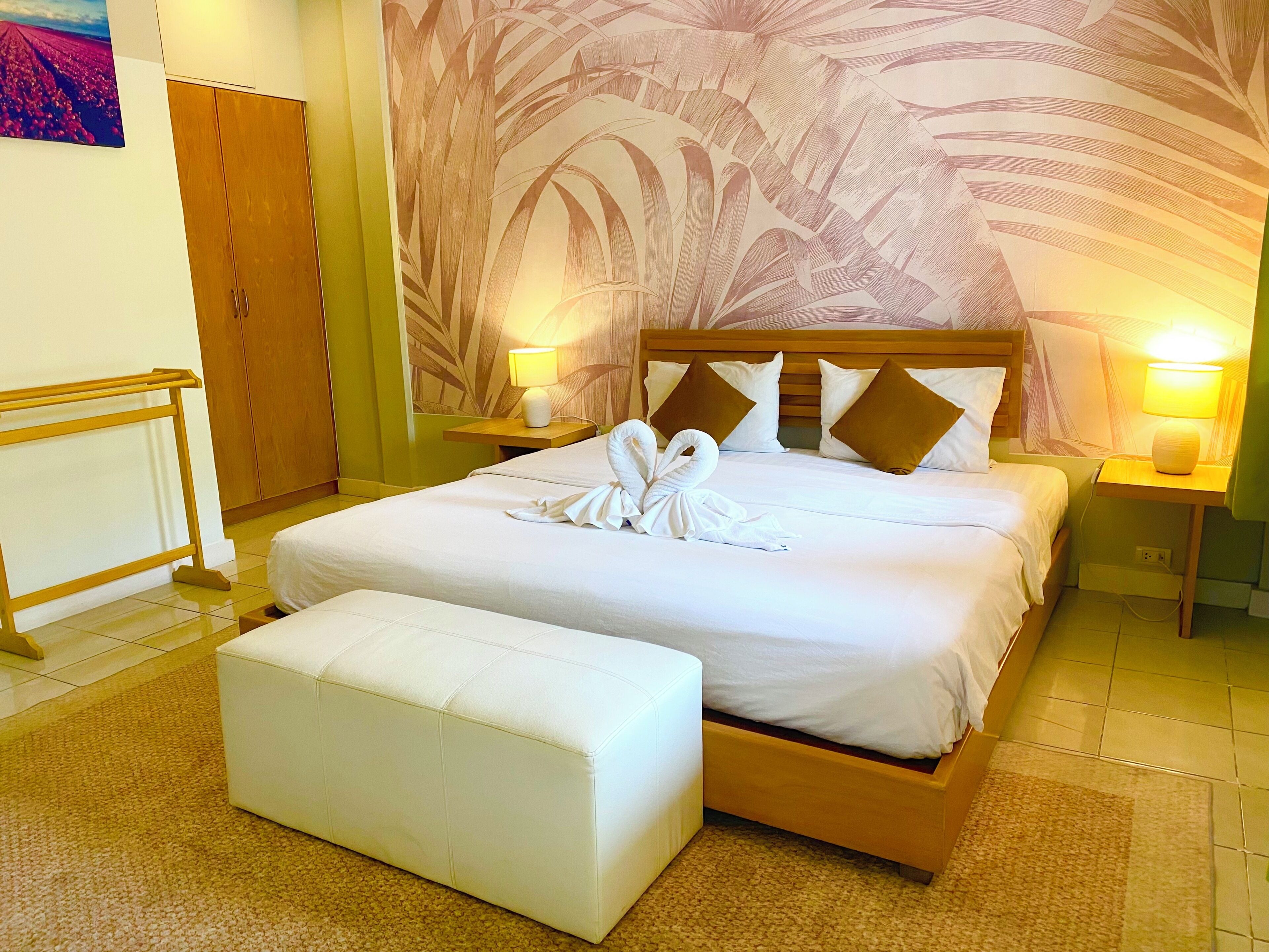 A neatly made bed with a towel arrangement, a wooden headboard, and a wall with a leaf pattern.