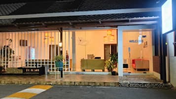 L’entrée d’un hôtel, avec un comptoir d’accueil, un panneau d’accueil et un espace détente agrémenté de plantes.