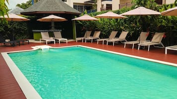 A swimming pool with lounge chairs and umbrellas, surrounded by greenery.