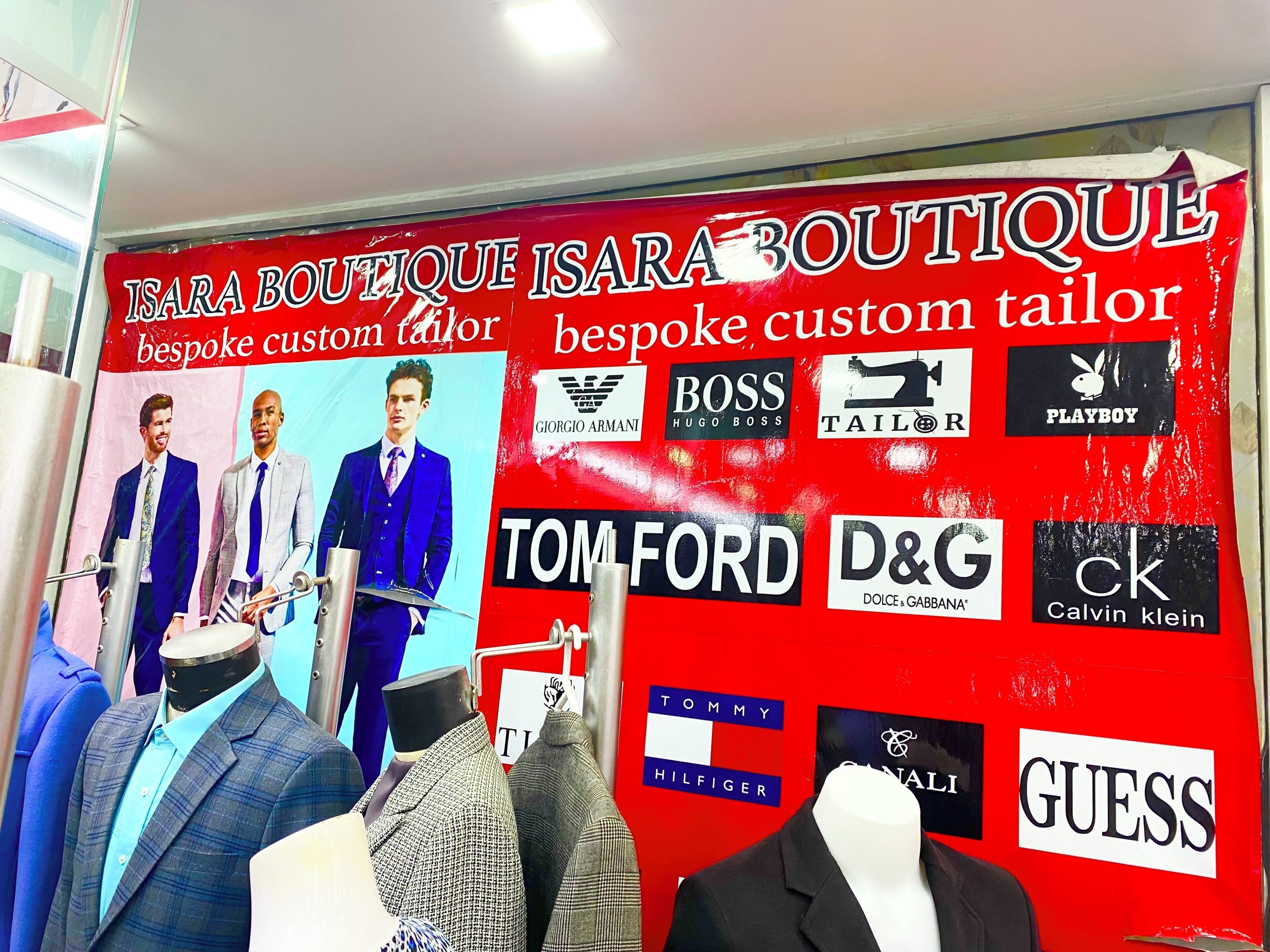 A boutique with mannequins displaying suits and a wall with various brand logos.