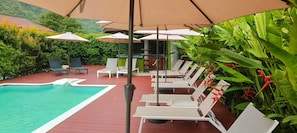 Un espace aménagé au bord de la piscine, avec des chaises longues et des parasols, le tout entouré de verdure.