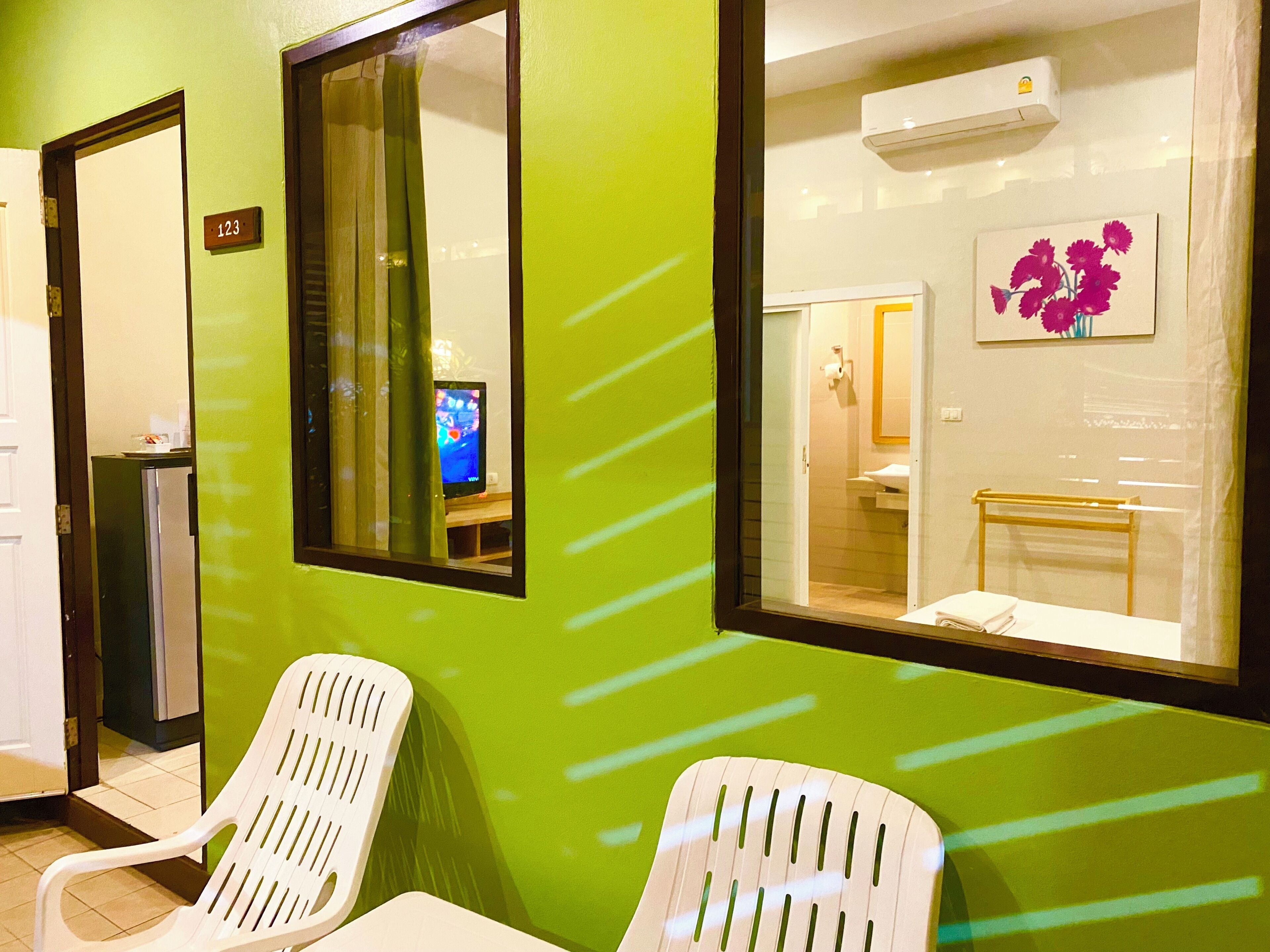 A room with a green wall, a window with a view of a bathroom, and two white chairs.