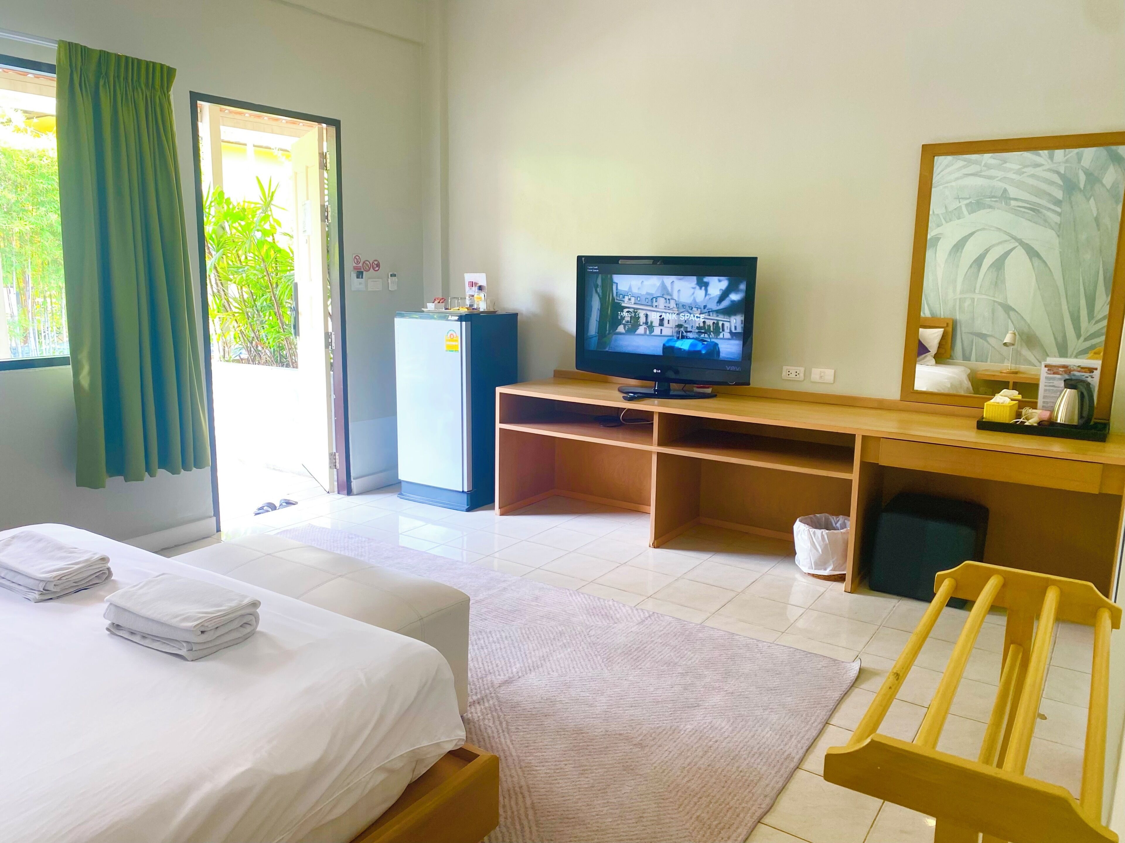 Ein Hotelzimmer mit einem Bett, einem Schreibtisch mit Fernseher, einem Kühlschrank und einem Fenster mit Vorhängen.