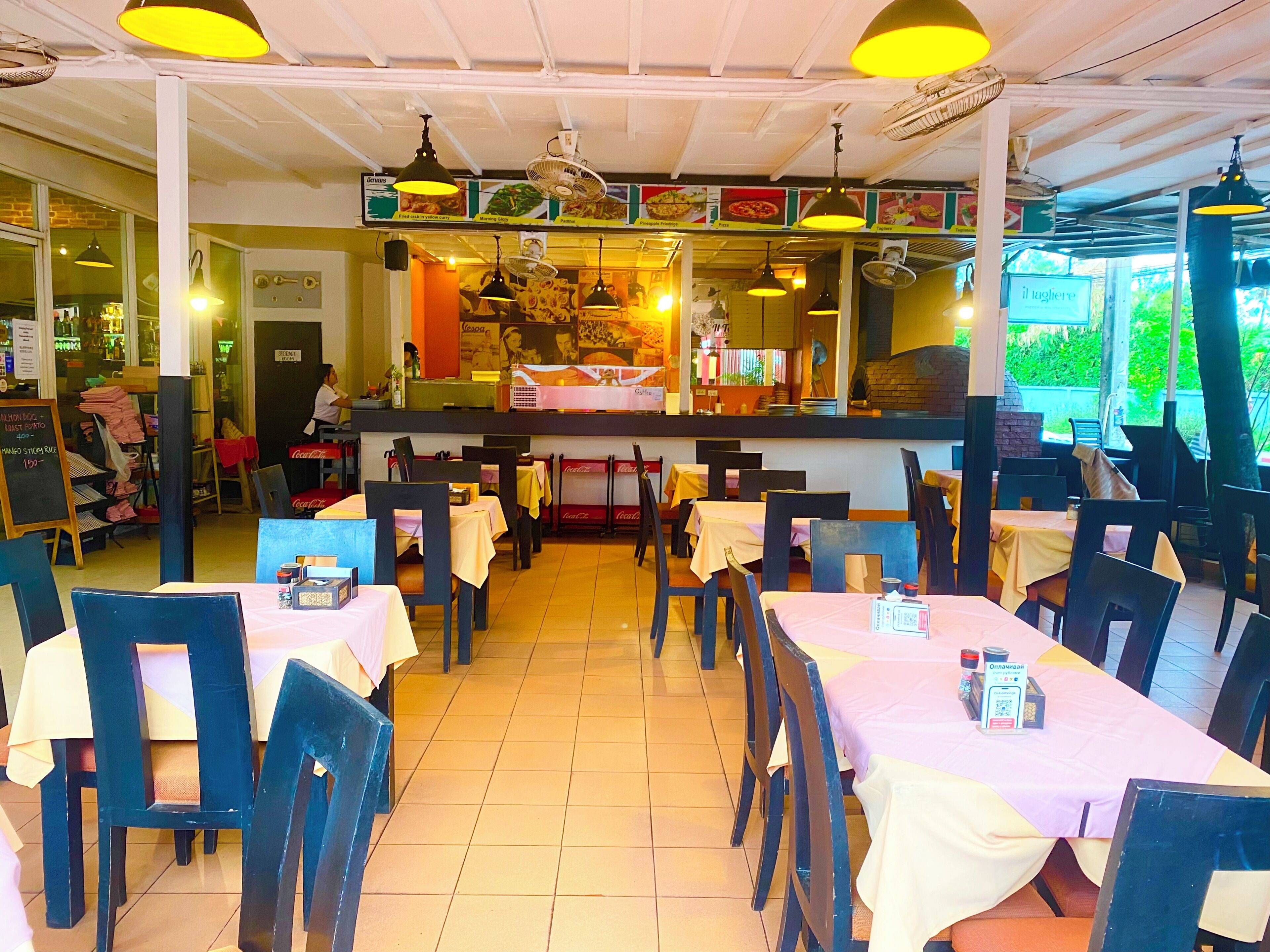 Interior de un restaurante con mesas y sillas, una barra con un menú y vistas al exterior.