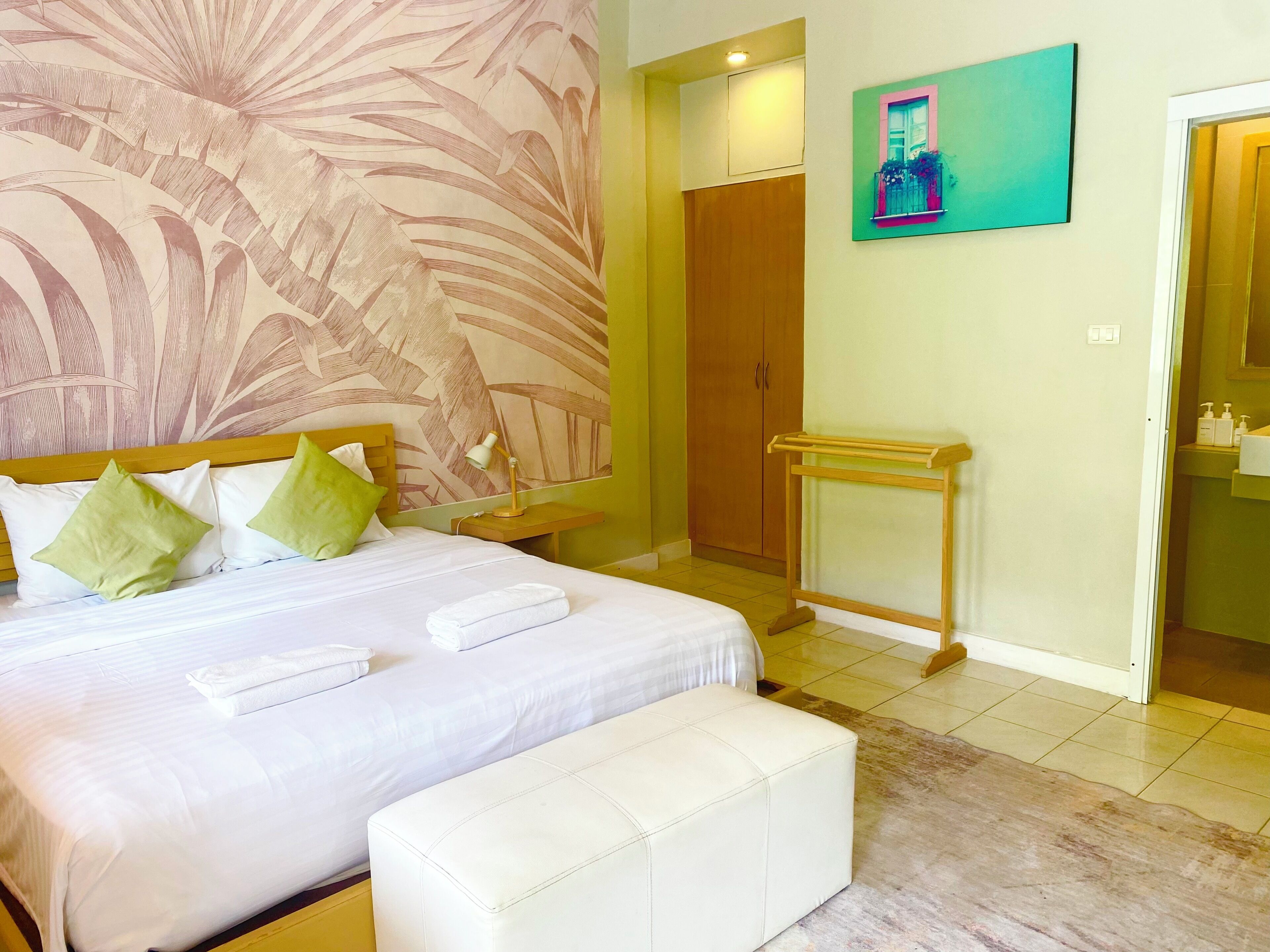 Une chambre d’hôtel avec un lit, une table de chevet avec une lampe, une armoire en bois, une salle de bain avec un lavabo et un tableau accroché au mur.