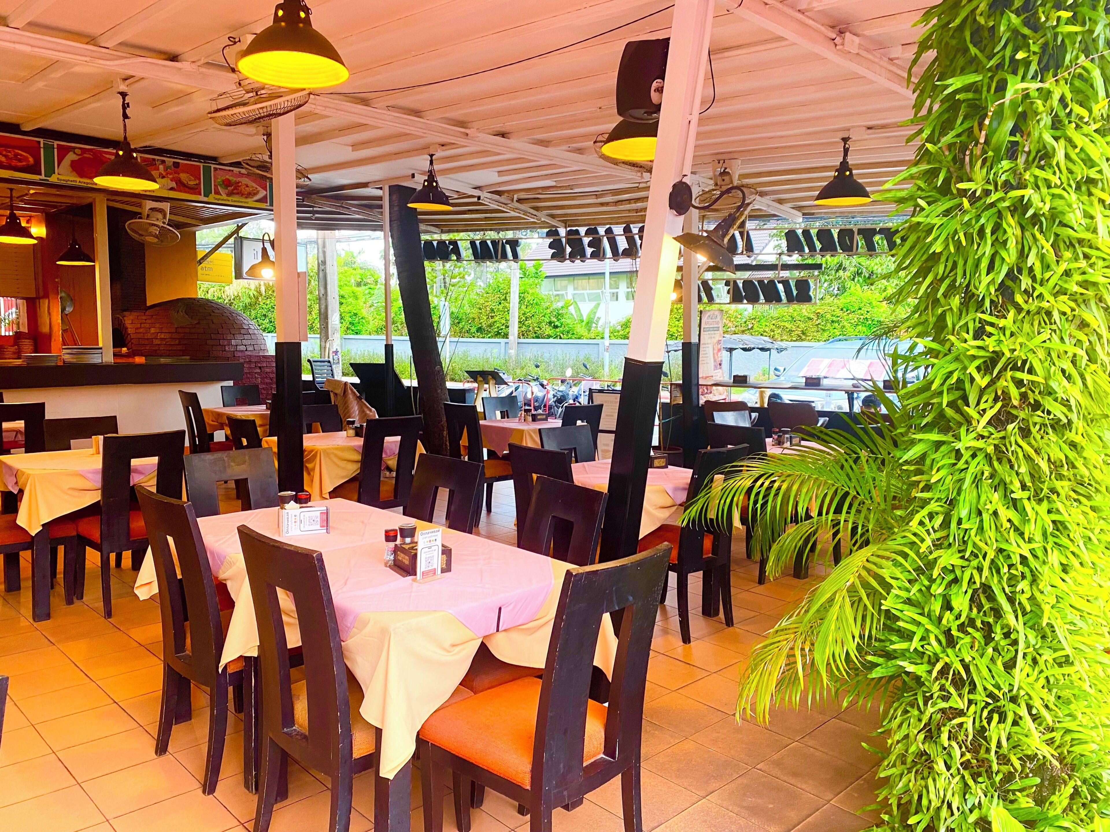 An indoor restaurant with tables and chairs, a pizza oven, and hanging lights.