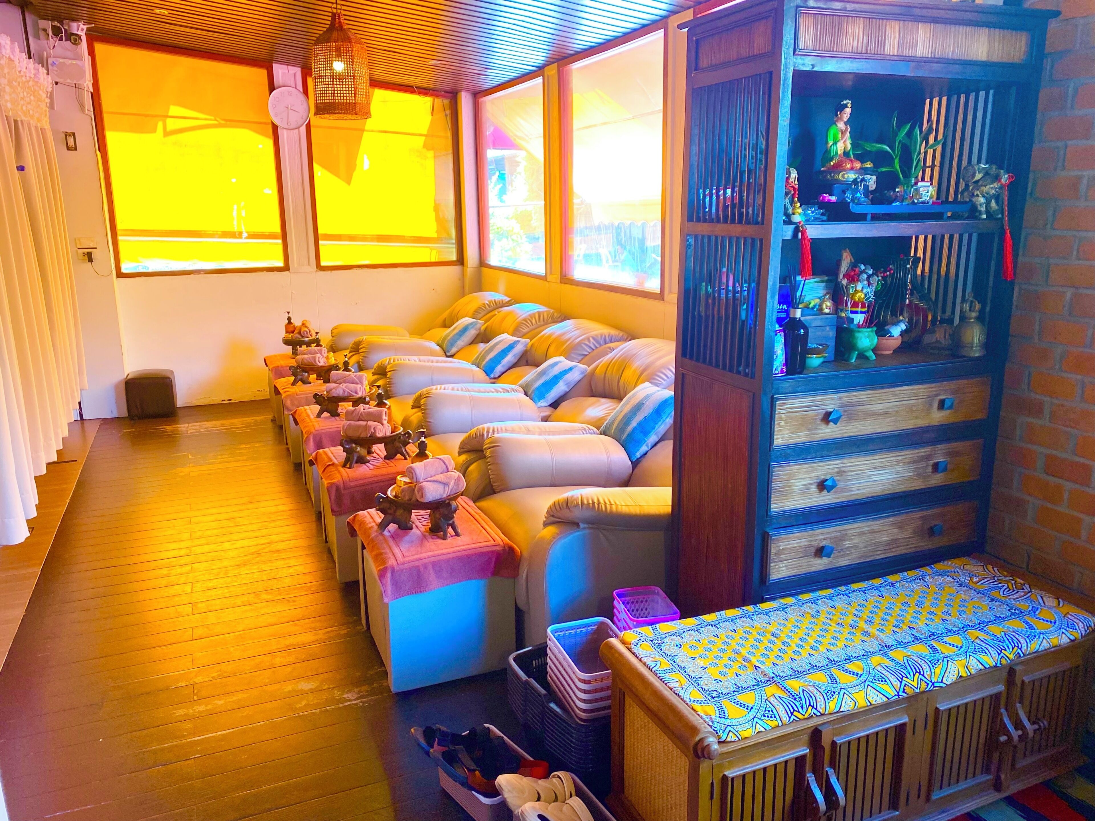 A room with multiple massage chairs, a wooden cabinet with decorative items, and a patterned tablecloth.
