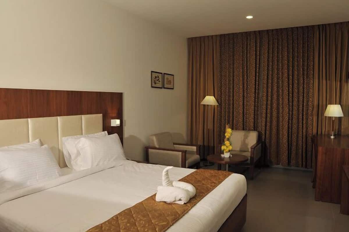 Ett hotellrum med en stor säng, ett trägaveltavla, ett litet runt bord med en lampa, en stol och ett skrivbord med en lampa.