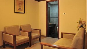 Una habitación con dos sillas de madera y un sofá, un cuadro enmarcado en la pared, y un baño visible a través de una puerta abierta.