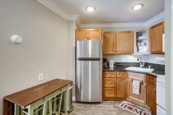 A kitchen with wooden cabinets, a stainless steel refrigerator, a wooden bench, and a welcome mat.