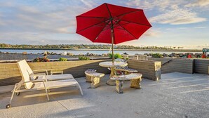 A rooftop terrace with a red umbrella, white lounge chairs, and stone tables. - Mission Beach Gem - 1BR Near the Ocean (San Diego)