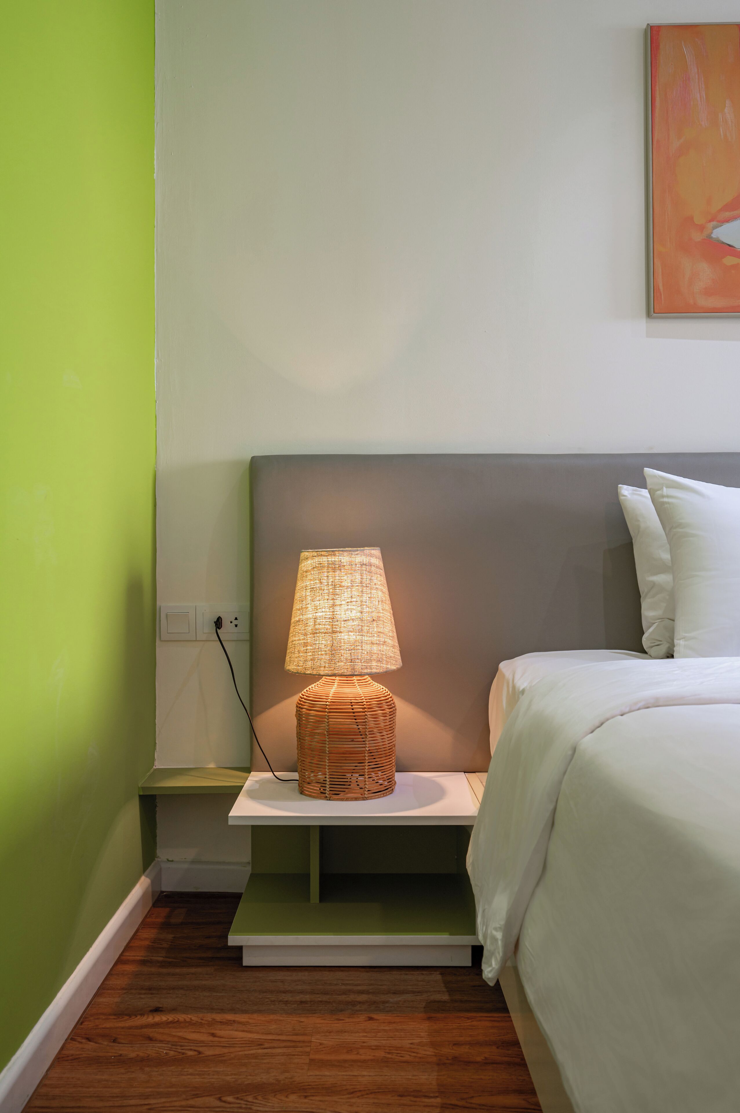 Un dormitorio ordenado con una lámpara de noche, una cama y una pared verde.