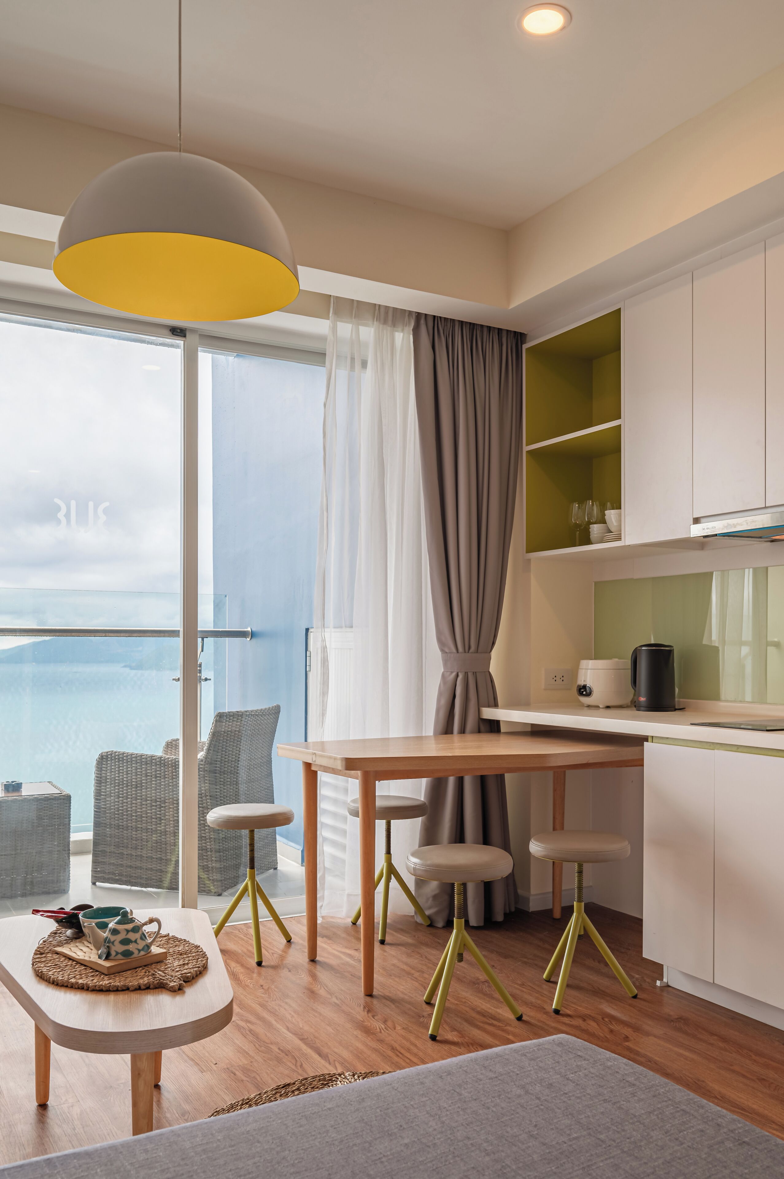 A modern kitchen with a dining area, a view of the sea, and a balcony with wicker furniture.