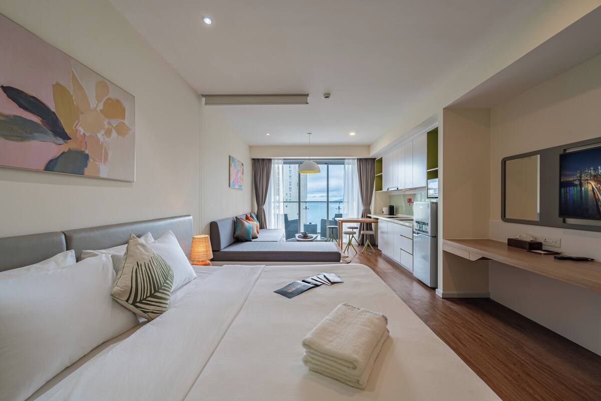 A modern hotel room with a large bed, a desk, a television, and a view of the city.